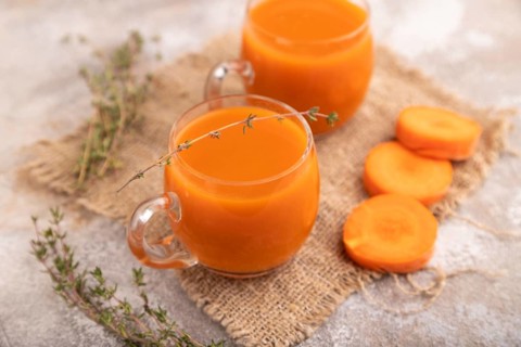 Two glasses with carrot juice, on brown concrete background and linen textile. Diet, healthy eating