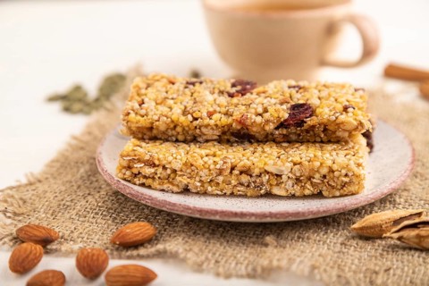 Granola bars with caramel, nuts, flakes in ceramic plate on white wooden background, beige linen