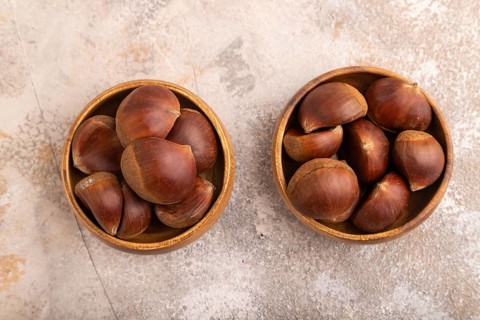 Wooden bowl with raw edible Ð¡hestnuts on brown concrete background, top view, flat lay, close up,