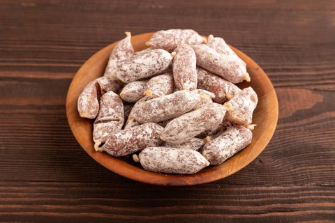 Small smoked Chicken sausages in wooden bowl on brown wooden background. side view, close up