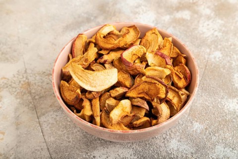 Dried Apples in ceramic bowl on brown concrete background. Side view, copy space, flat lay. healthy