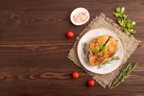Fried Turkey Thigh with spices and rosemary on plate on brown wooden background and linen textile.