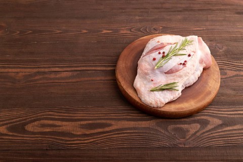 Raw Turkey Thigh with spices and rosemary on cutting board on brown wooden background. side view,