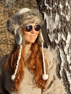 Slender pretty woman with fur hat and pompoms, red hair and warm winter colors between birch forest