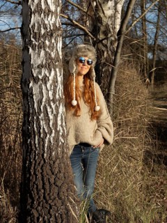 Slender pretty woman with fur hat and sweater, red hair and warm winter colors between birch forest