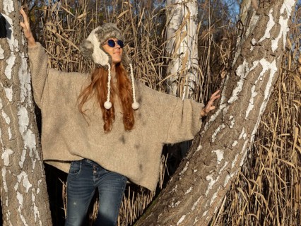 Slender pretty woman with fur hat and sweater, red hair and warm winter colors between birch forest