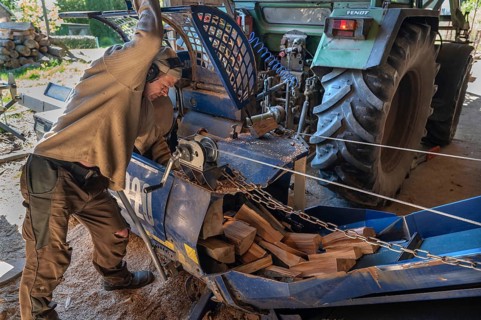 Young man sawing and splitting beech logs with his saw cutting machine, powered by a tractor in a
