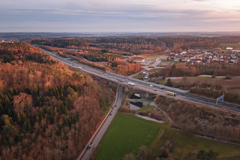 Aerial view of road junction in rural areas, lined with dense forest and visible traffic flow, A8