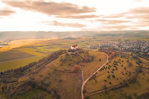A hill with a church and a wide view over fields and a village under a cloudy sky, Wurmlinger