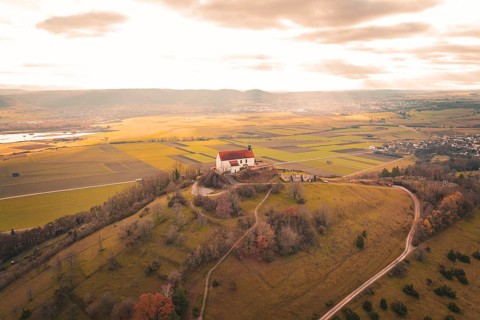 Panoramic view of a church on a hill with surrounding fields and vast clouds, Wurmlinger Chapel,