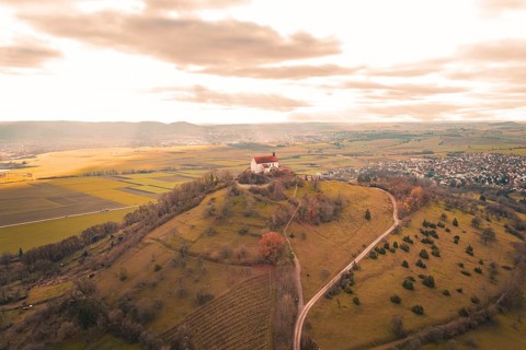 A church on a hill with a wide view of fields and villages under a cloud cover, Wurmlinger Chapel,