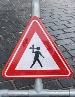 Triangular warning sign on cobblestones depicting a stylized figure with a tray, province of
