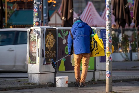 Man sticks posters to electrical boxes near Alexanderplatz, Berlin, Germany
