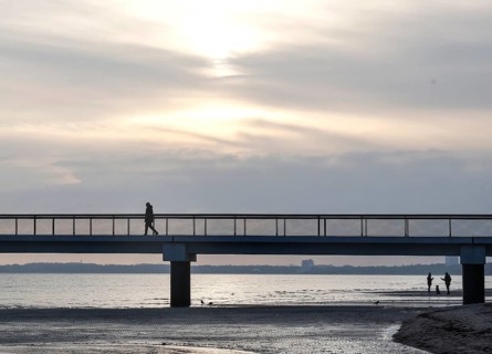 Silhouettes of people on and under a pier, low tide, wave and ripple patterns in wet sand, sunrise,