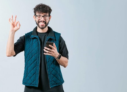 Attractive man in glasses holding phone gesturing OK. Smiling handsome man holding phone and