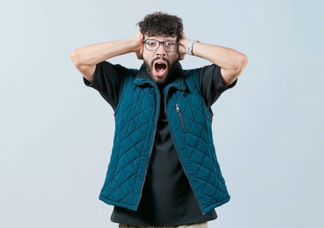 Panicked young man holding her head isolated. Worried and alarmed man holding her head