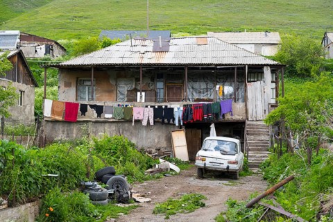 Rural house with clothesline and old car nestled in green landscape with hills, poor house in