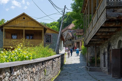 Village street lined with old buildings with wooden verandas flanked by green vegetation under a