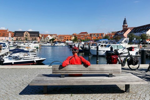 Cyclist with helmet, sitting on a wooden bench, e-bike with luggage bags, bike tour, boats in the