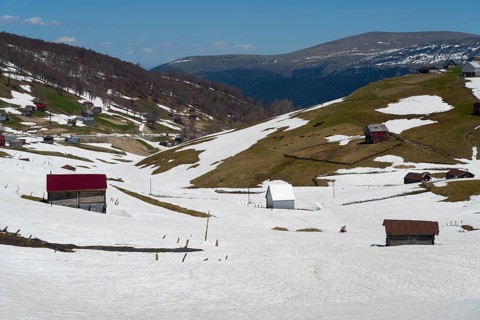 Snowy hills with scattered buildings and valleys in a mountainous landscape, view from Goderdzi