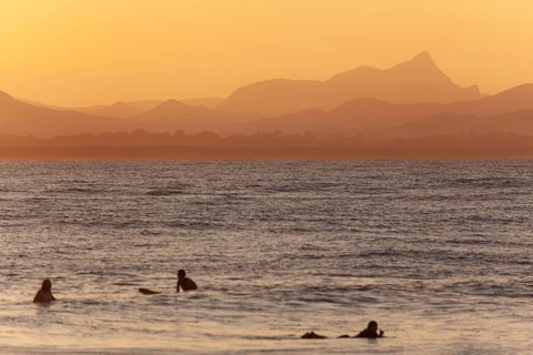 Red sunset on Wategos Beach with surfers in the ocean. Mt. Warning, Wollumbin in the background of