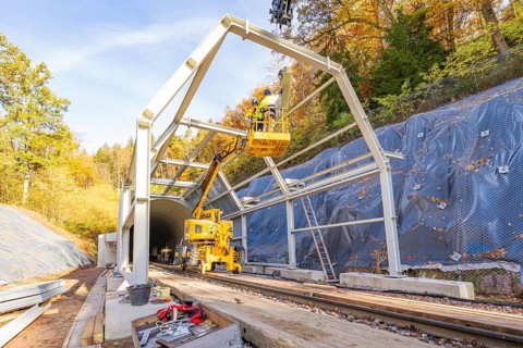 Construction work on a tunnel opening with cranes and workers against an autumn backdrop, Hermann