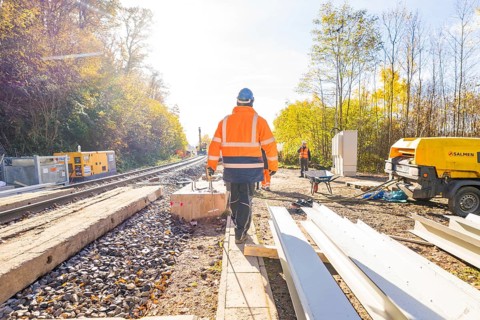 Construction workers in glowing vests work on a railway construction site under clear skies,