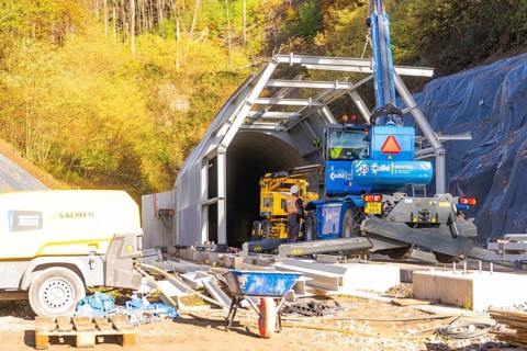 Construction site in front of a tunnel with machinery surrounded by autumn trees, Hermann Hesse