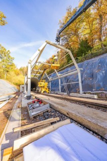 Crane lifts construction material for a tunnel surrounded by autumnal forest and blue skies,