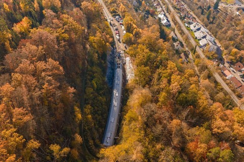 Aerial view of a construction site in colorful autumn forest with adjacent roads and houses,