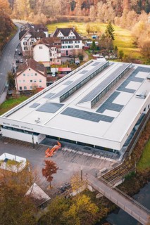 Building with solar panels surrounded by village houses and autumn trees, PV at Walther Lindner