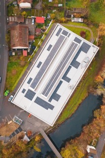 Building with solar roof, surrounded by a village and river, viewed from the air in an autumn