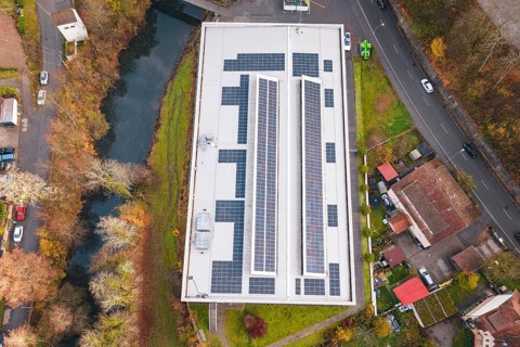 Aerial view of a building with solar panels, surrounded by river and roads, PV at Walther Lindner