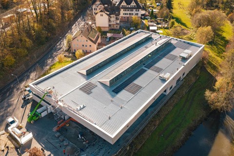 Modern building with solar panels, surrounded by a river and autumnal nature, viewed from the air,