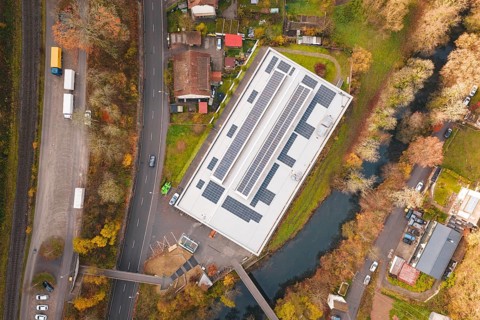 Aerial view of a building with solar panels, surrounded by river and trees, PV at Walther Lindner