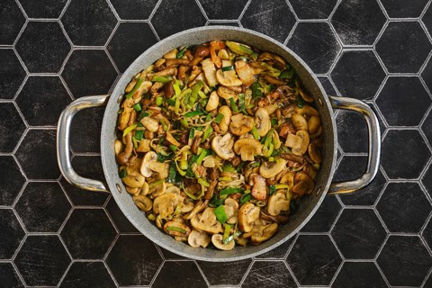 Freshly cooked mushrooms and onions are sautÃ©ed in a large skillet. Green leek add flavor. The