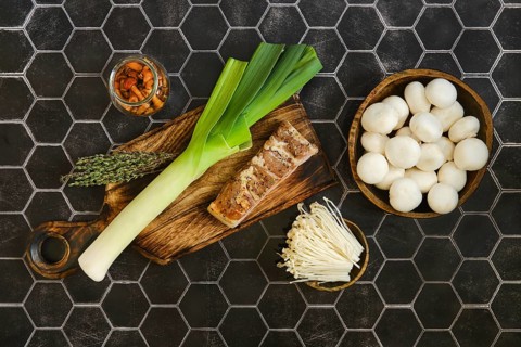 Fresh leeks, bacon and thyme on a wooden cutting board. A jar of pickled honey mushrooms and fresh