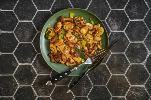 Mushroom stir fry is arranged on a green plate, featuring a mix of fried mushrooms and leek. The
