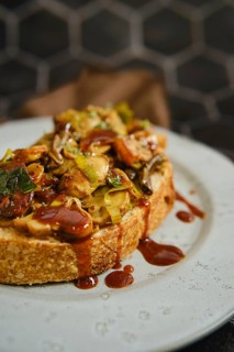 A warm mushroom sandwich is served on a rustic plate, topped with honey mushrooms, enoki mushrooms,