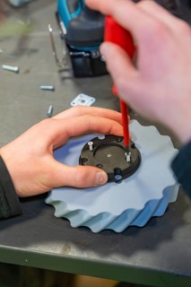 Screwdriver fixes screws to a gear wheel in a workshop environment, Jugend Forschungszentrum