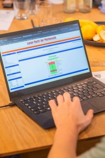Hand operates a laptop with mathematics software on a wooden table, Jugend Forschungszentrum