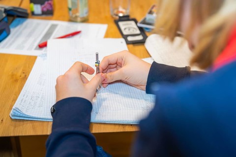 Person writing notes on checkered paper at a wooden table, Jugend Forschungszentrum Nagold, Calw