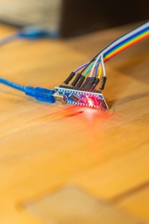 Red glowing circuit board connected to USB cable on wooden table, Jugend Forschungszentrum Nagold,