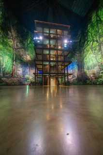An artificial jungle installation with a green illuminated wooden tower in a hall, Amazonia