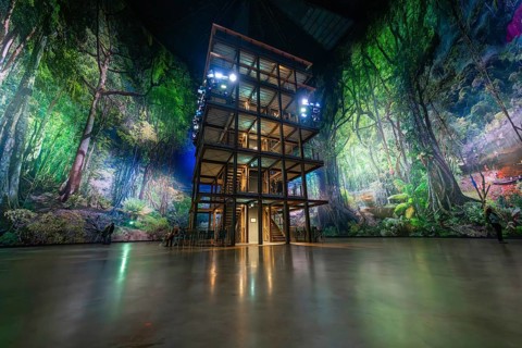 A multi-storey timber building in a glowing green artificial forest installation, Amazonia