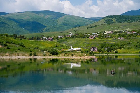 Lakeside village with mountains in the background, calm water with reflection, Tu-134A aircraft as