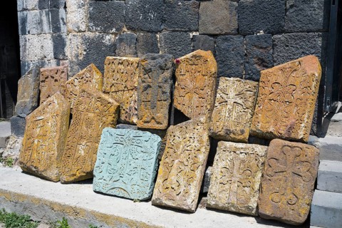 Decorated, engraved tombstones lean against an old wall, cross stones at Sevanavank Monastery,