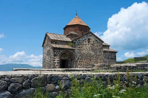 Historic stone church with orange roof against blue sky and white clouds, Sevanavank Monastery,