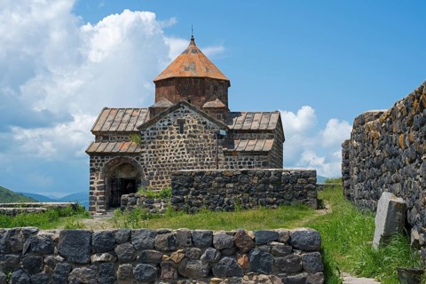 Front view of a historic stone church with brick wall and overgrown landscape, Sevanavank