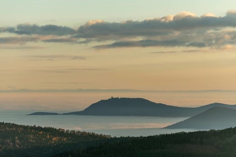 The landscape of hills and mountains is illuminated by a gentle sunset. Sea of fog in distance